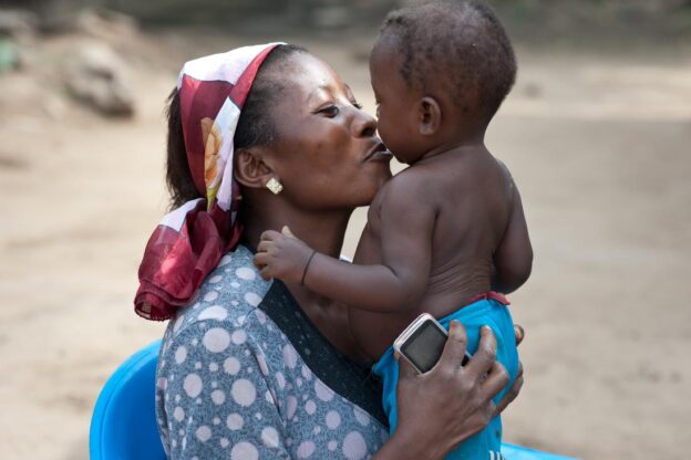 A women of colour smiles as she kisses her young baby.